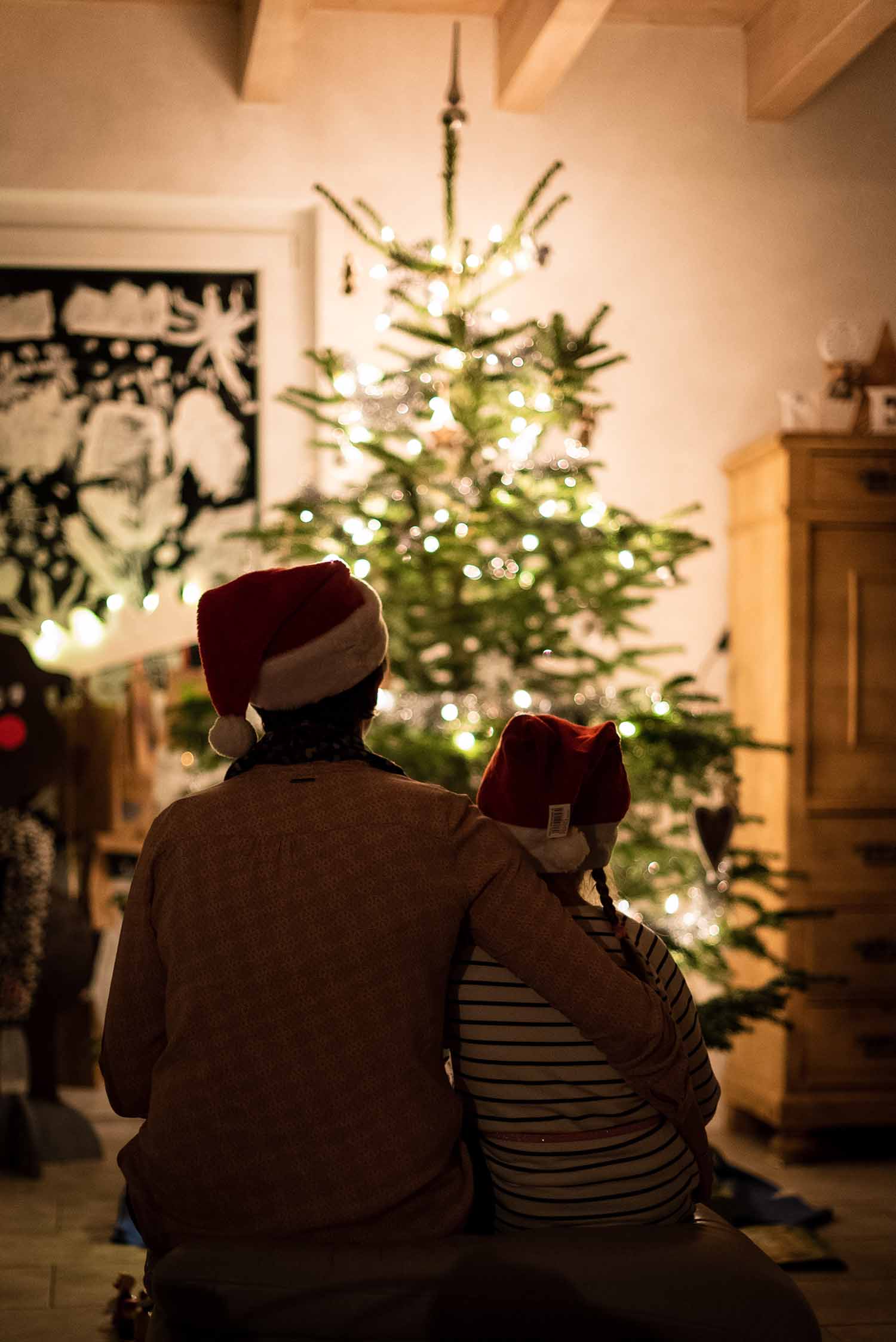 a person and child wearing santa hats and standing in front of a christmas tree